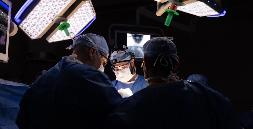 Dr. Tyler McDonald, pediatric orthopaedic surgeon and an assistant professor of orthopaedic surgery, center, and Dr. Richard Menger, chief of complex spine surgery and associate professor of neurosurgery, right, perform surgery at USA Health Children’s & Women’s Hospital in August 2023 to insert pins into Abby Flowers's skull for halo gravity traction.